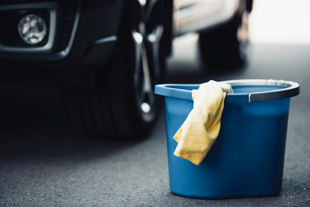 blue-bucket-and-yellow-rag-on-asphalt-near-black-car