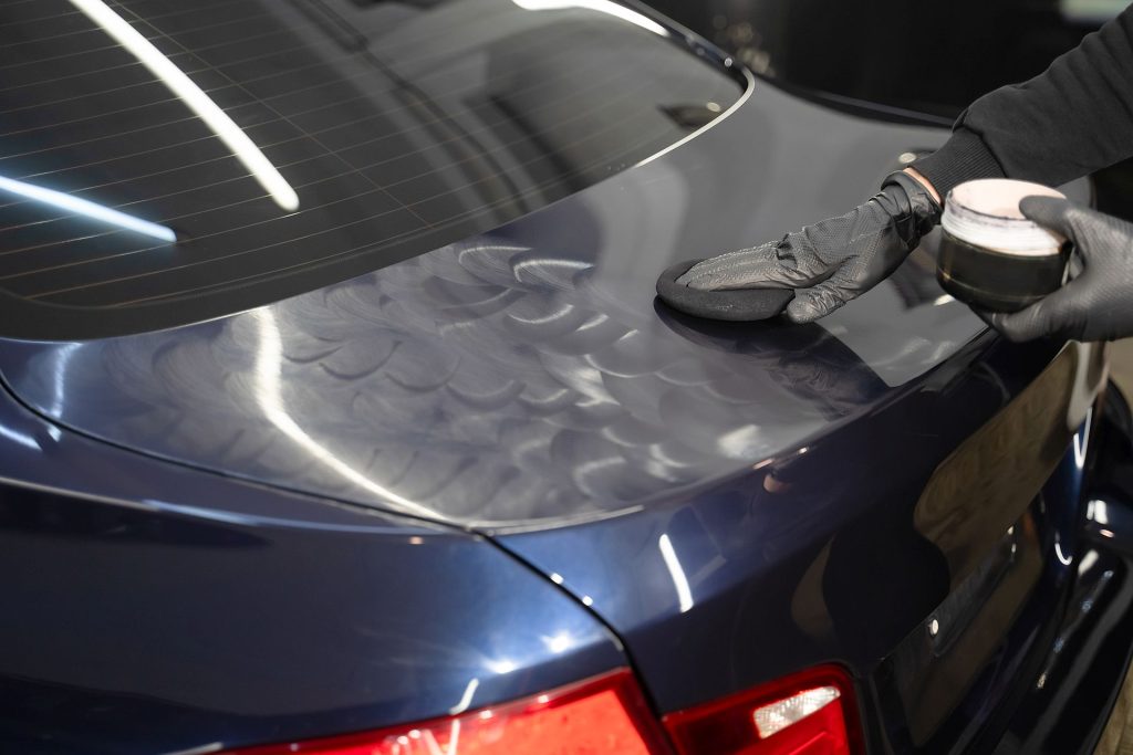 auto detailer hand applying wax to the trunk lid of a car